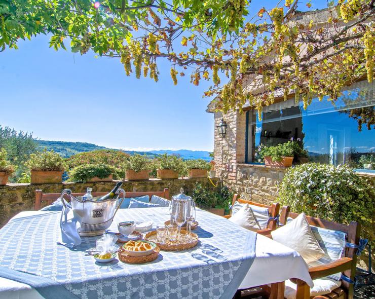 Sunny terrace with set table, view of green hills and blue sky.